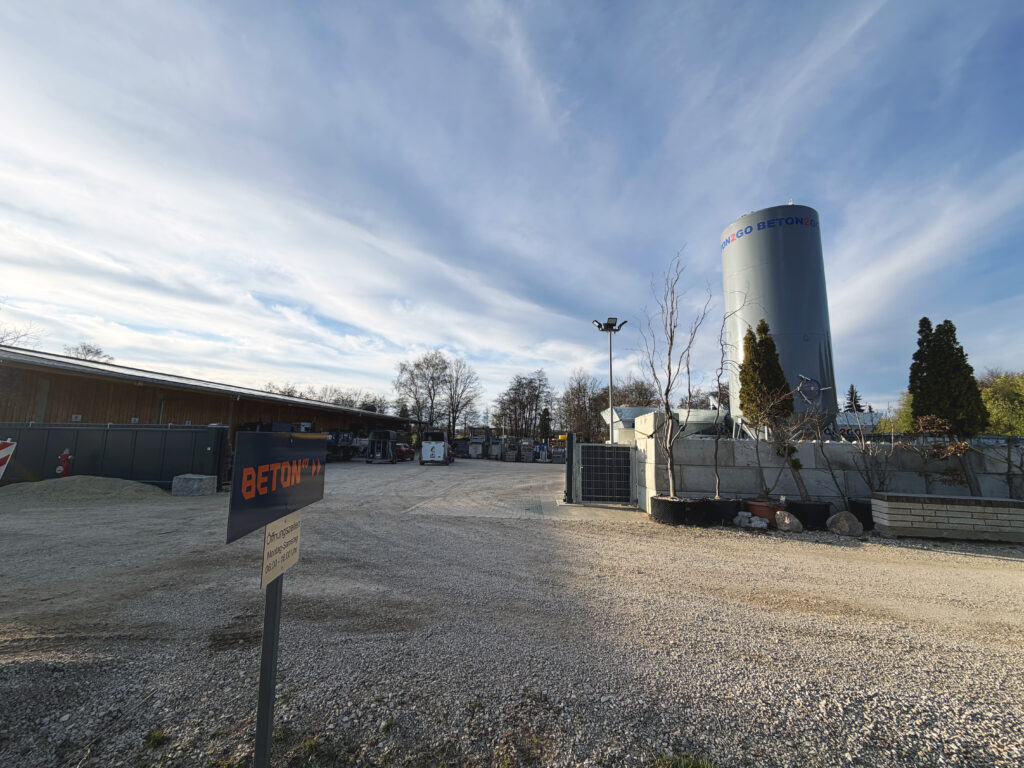 Blick auf einen Wegweiser mit dem Logo Beton4U und der Betontankstelle im Hintergrund.